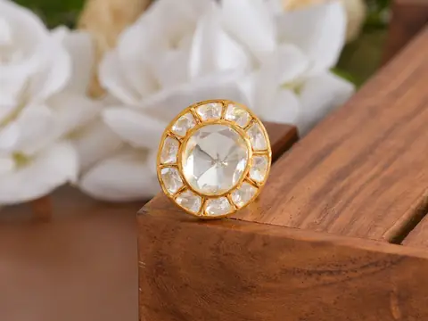 A gold ring with a flat-cut diamond on a wooden block beside white roses
