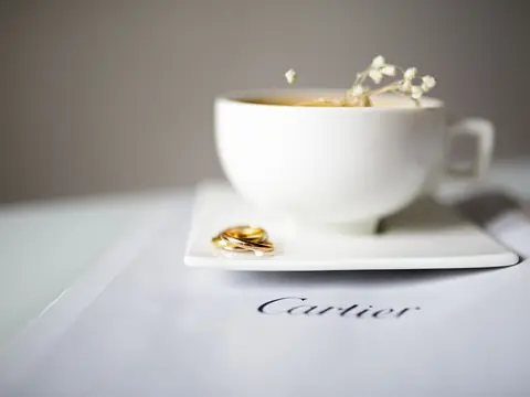 A gold ring resting by a Cartier card under a white porcelain cup