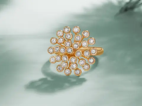 A gold flower ring set with round diamonds on a pale teal ground