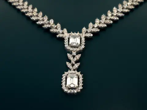 A diamond necklace with an emerald-cut pendant on a deep green ground
