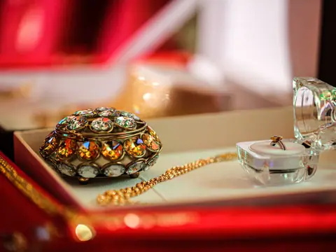 An ornate jeweled box, gold chains and rings in a red display case