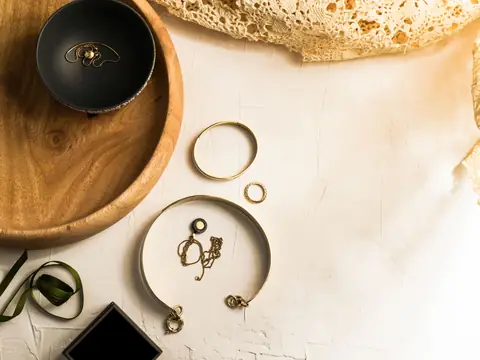 Gold bangles, rings and charms around a wooden dish on white plaster