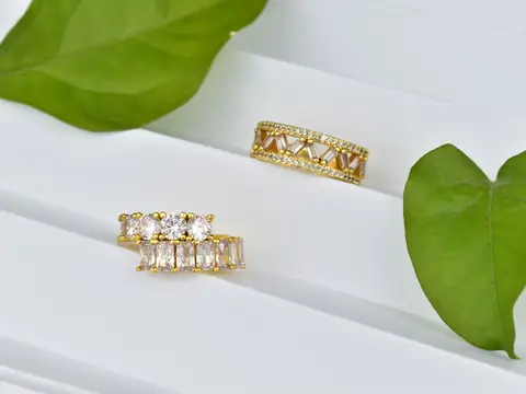 Two gold rings set with baguette and round diamonds on white slats with green leaves