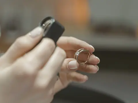 A hand holding a jeweler's loupe beside a diamond ring