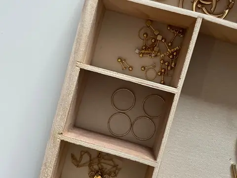 An open wooden jewelry box holding gold hoop earrings, chains and rings