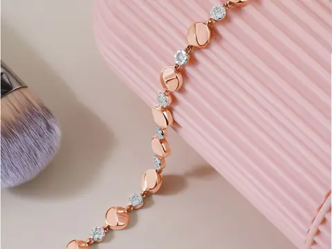 A rose gold bracelet set with diamonds draped over a pale pink ribbed stand