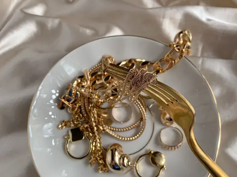 Gold chains, rings and earrings heaped on a white porcelain plate on cream satin