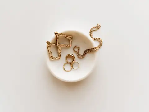 Gold hoop earrings, rings and a rope chain in a white marble dish