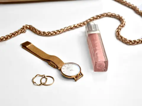 A gold chain, a gold mesh watch and two thin rings on a white surface