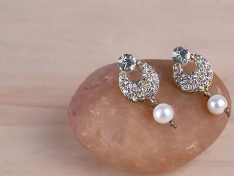 Diamond crescent earrings with pearl drops resting on a smooth pink stone